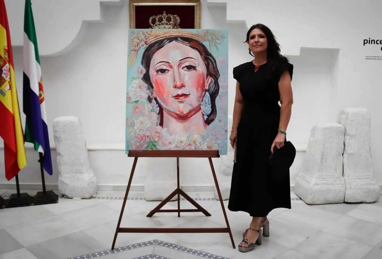 Nuria Hurtado, junto al cartel que pintó para las Fiestas del Carmen de Salteras de 2026, en la imagen difundida por la Unión de Hermandades para anunciar su nombramiento.